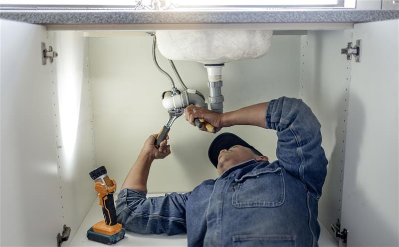 Plumber repairing pipes beneath a bathroom sink in Fair Oaks